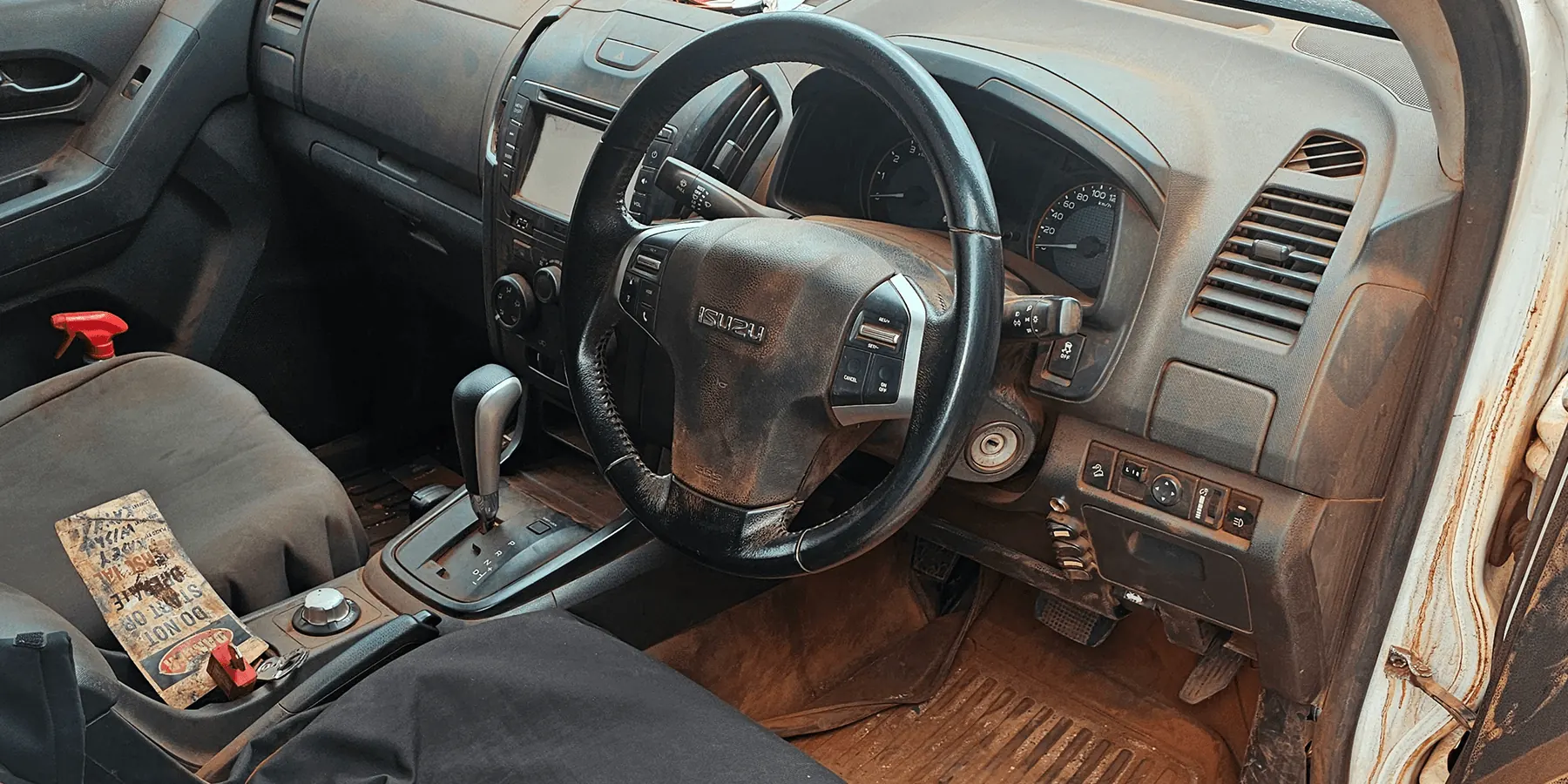 Dusty and dirt-covered Isuzu D-MAX cabin interior with red Kimberley dust on floor and dashboard before interior detailing by Kimberley Auto Care