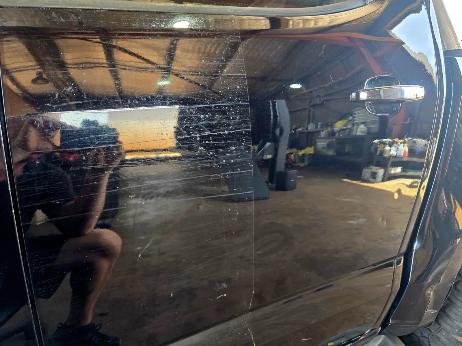 Close-up of black vehicle panel showing heavy swirl marks, scratches and water spots before paint correction by Kimberley Auto Care