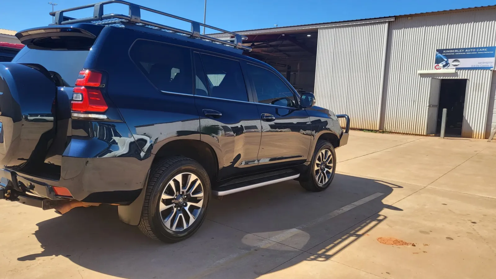 Black Toyota LandCruiser Prado with roof rack and dark tint - detailed to mirror finish outside Kimberley Auto Care workshop in Broome